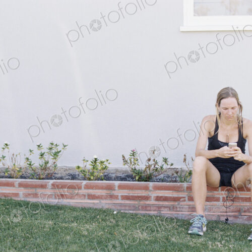 Blond woman in sportswear sitting on a garden wall, resting after a jog.