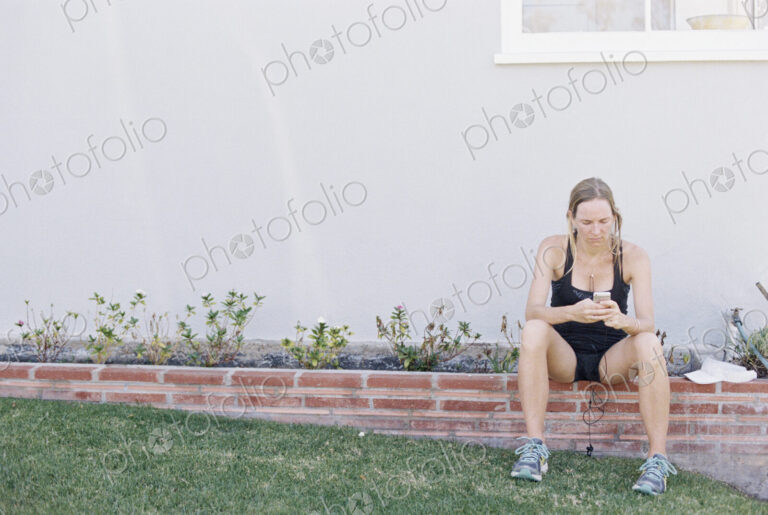 Blond woman in sportswear sitting on a garden wall, resting after a jog.