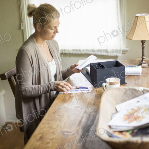 Blond woman sitting at a desk by a window, looking at photographs.