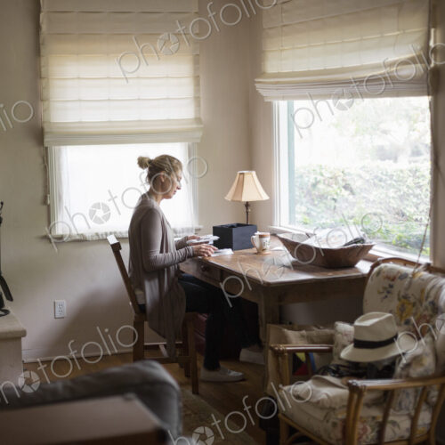 Blond woman sitting at a desk by a window, looking at photographs.