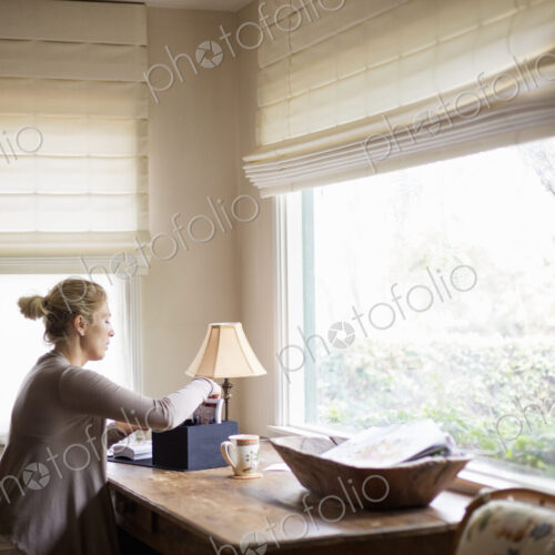 Blond woman sitting at a desk by a window, sorting through a box with photographs.