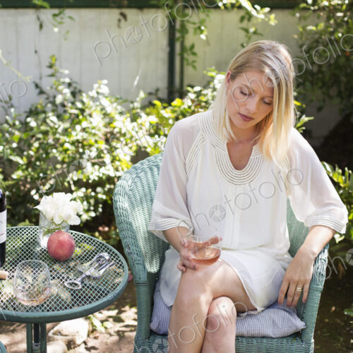 Blond woman sitting in a garden in summer, holding a wine glass.