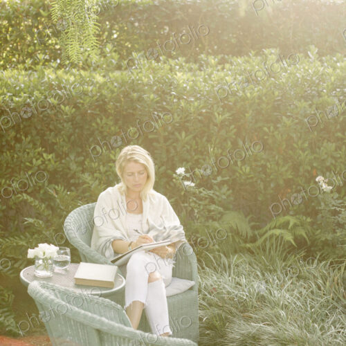 Blond woman sitting in a wicker chair in a garden.