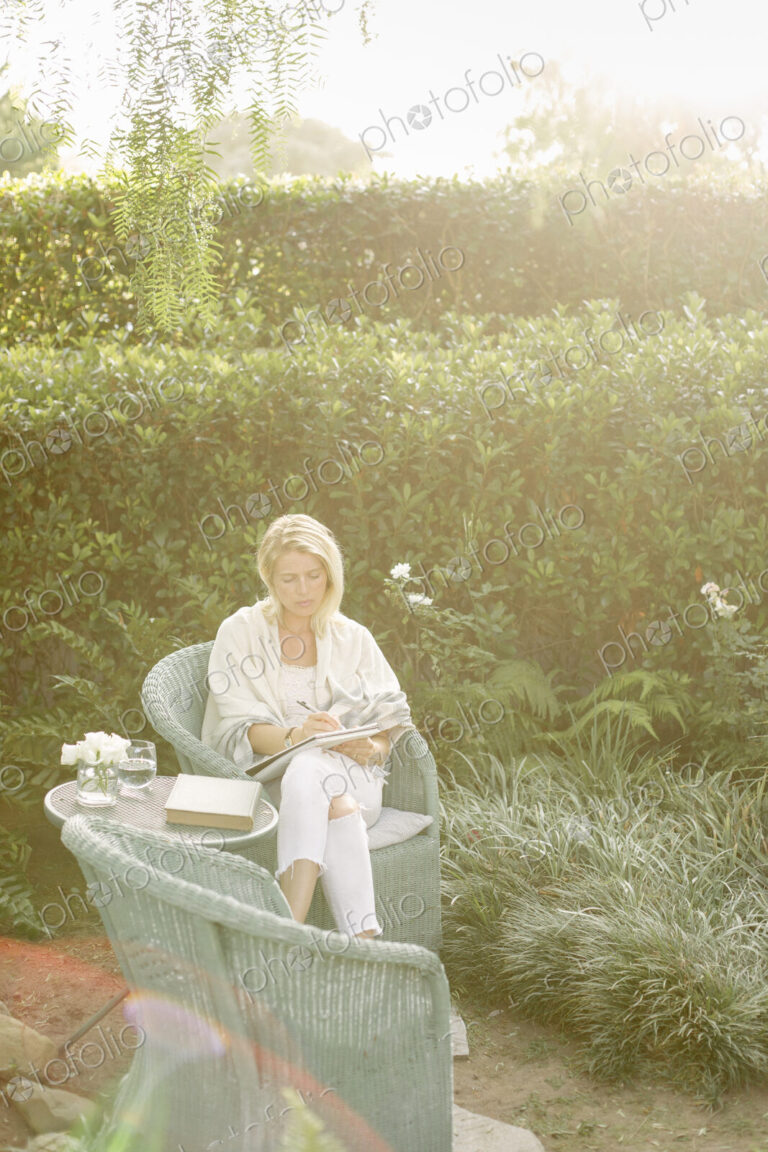Blond woman sitting in a wicker chair in a garden.