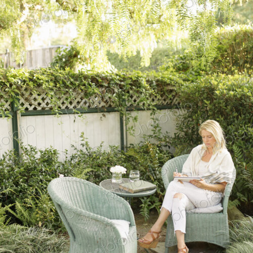 Blond woman sitting in a wicker chair in a garden.