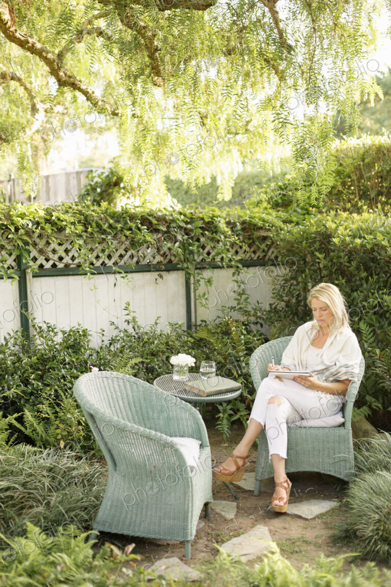 Blond woman sitting in a wicker chair in a garden.