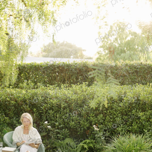 Blond woman sitting in a wicker chair in a garden.