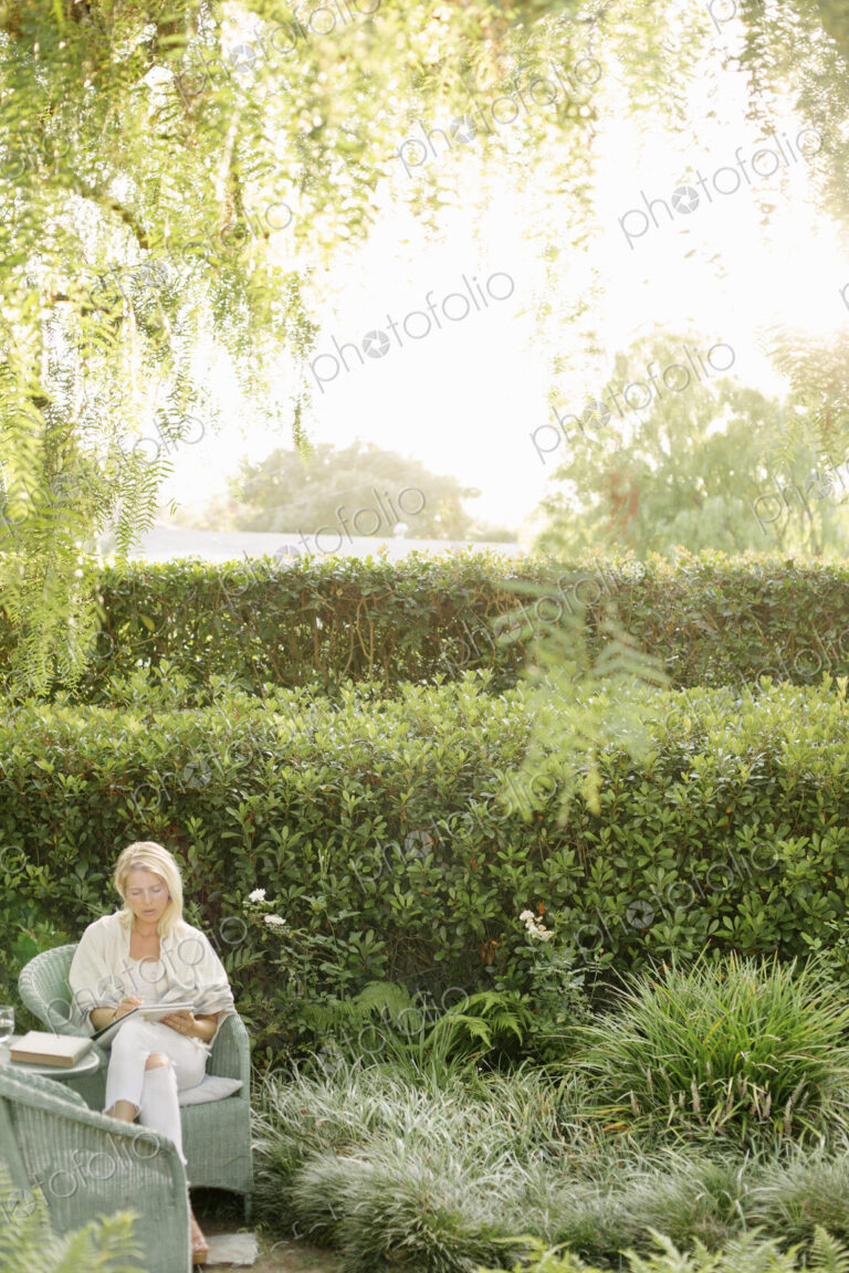 Blond woman sitting in a wicker chair in a garden.
