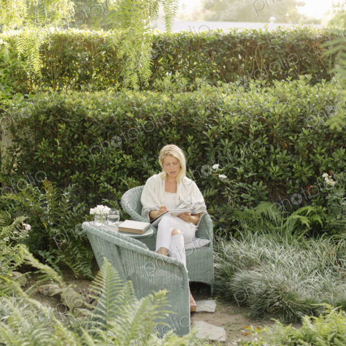 Blond woman sitting in a wicker chair in a garden.