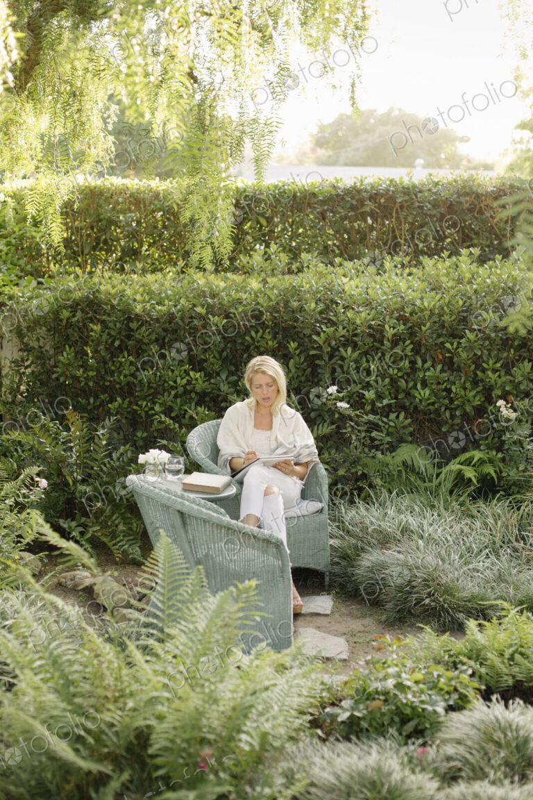 Blond woman sitting in a wicker chair in a garden.