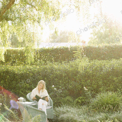 Blond woman sitting in a wicker chair in a garden, reading. Blond woman sitting in a wicker chair in a garden, reading.