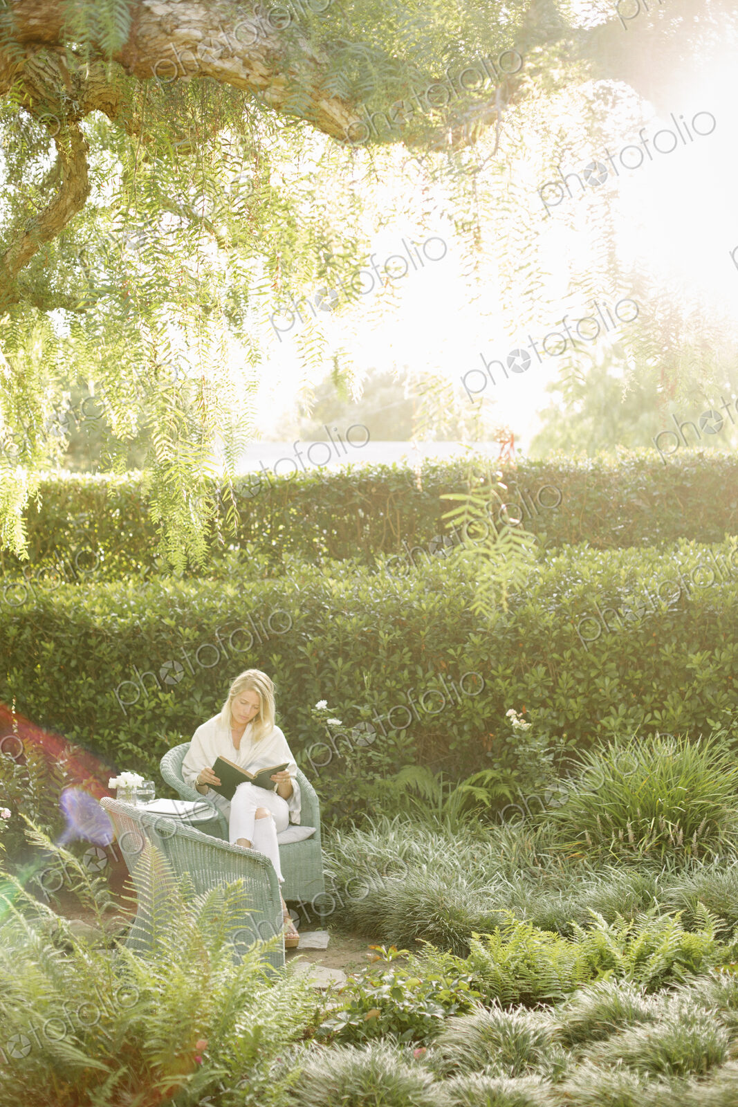 Blond woman sitting in a wicker chair in a garden, reading.