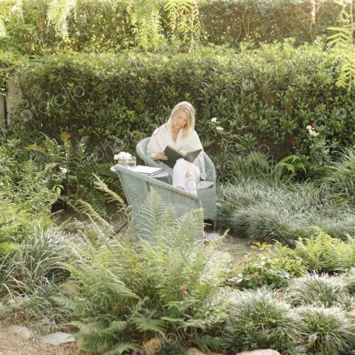 Blond woman sitting in a wicker chair in a garden, reading. Blond woman sitting in a wicker chair in a garden, reading.