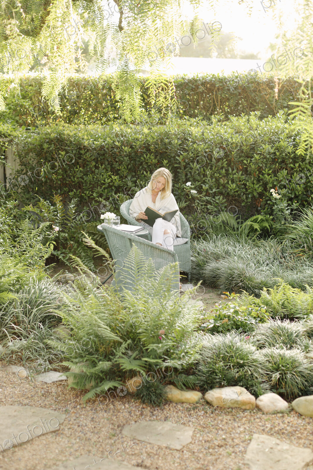 Blond woman sitting in a wicker chair in a garden, reading.