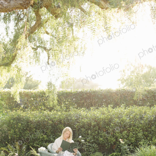 Blond woman sitting in a wicker chair in a garden, reading. Blond woman sitting in a wicker chair in a garden, reading.