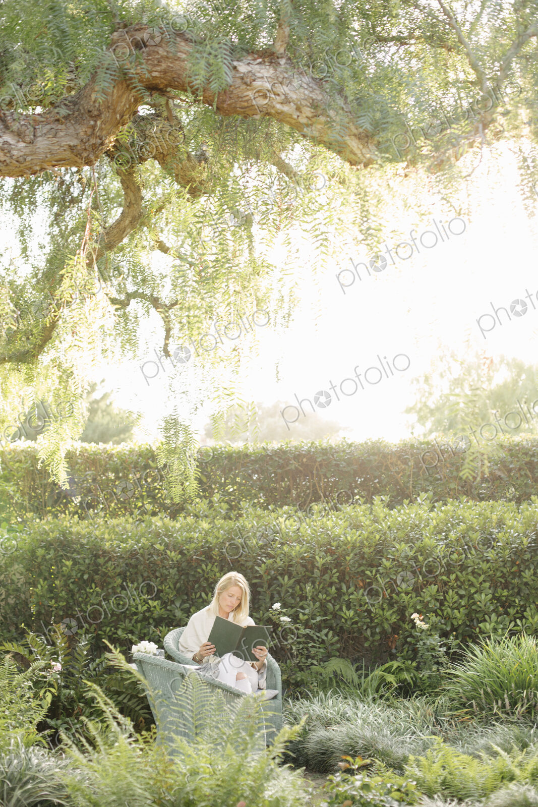 Blond woman sitting in a wicker chair in a garden, reading.
