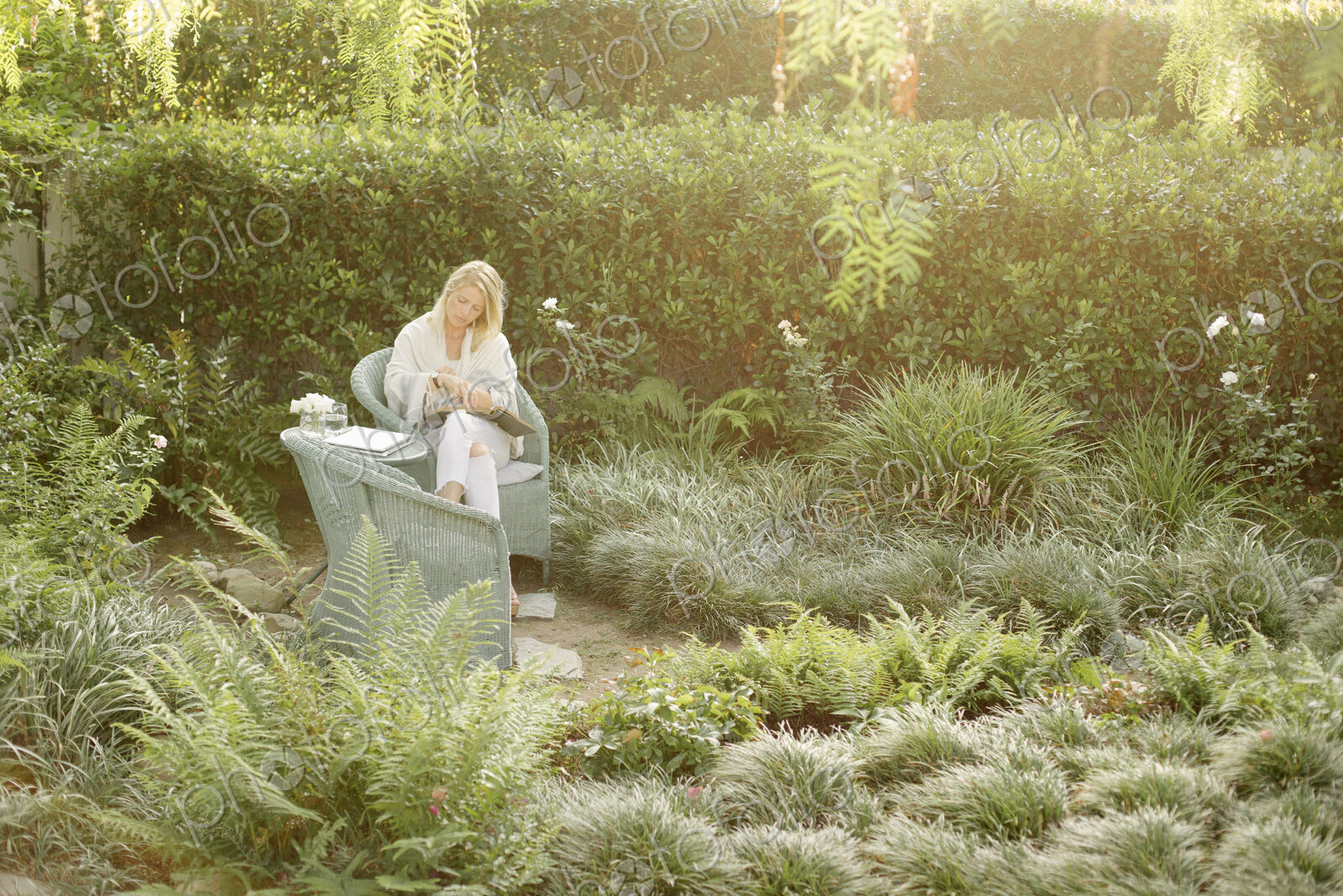 Blond woman sitting in a wicker chair in a garden, reading.