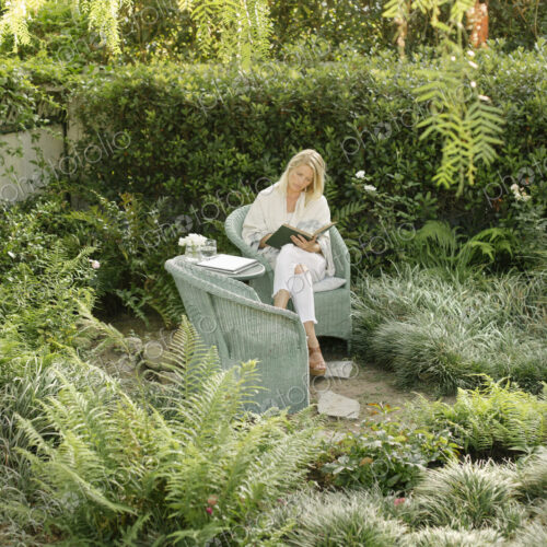 Blond woman sitting in a wicker chair in a garden, reading. Blond woman sitting in a wicker chair in a garden, reading.