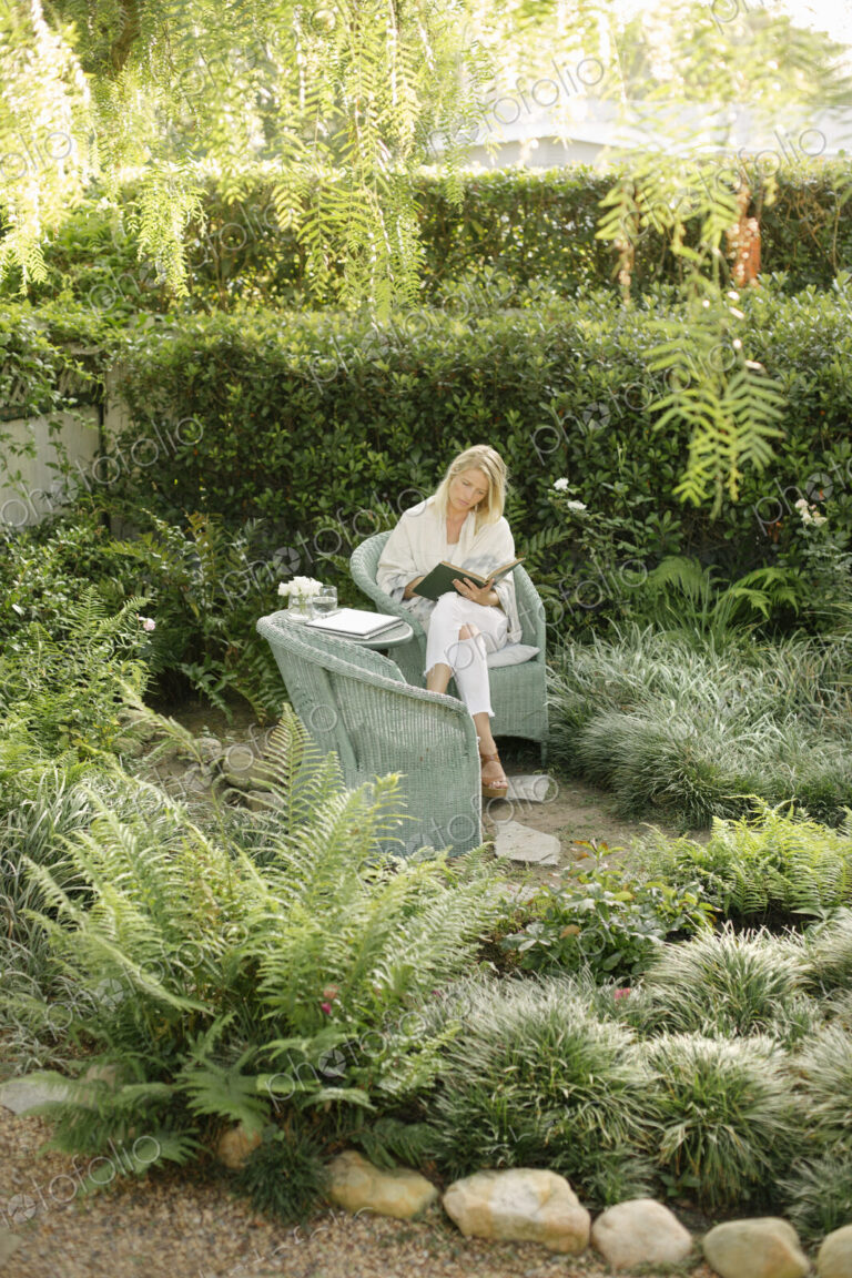Blond woman sitting in a wicker chair in a garden, reading.