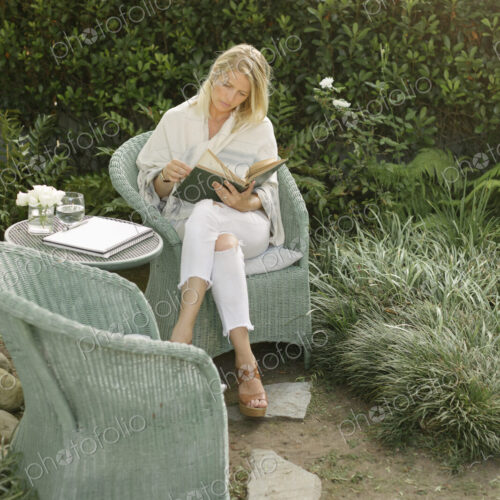 Blond woman sitting in a wicker chair in a garden, reading. Blond woman sitting in a wicker chair in a garden, reading.
