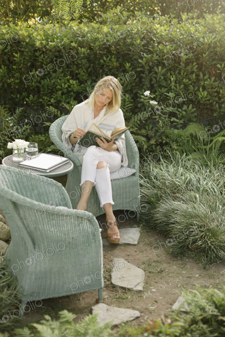 Blond woman sitting in a wicker chair in a garden, reading.