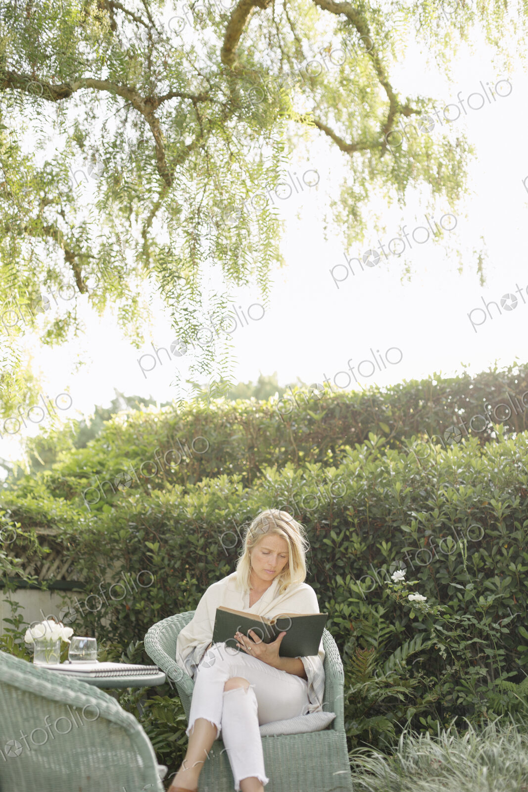 Blond woman sitting in a wicker chair in a garden, reading.