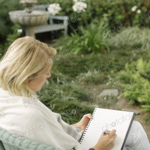 Blond woman sitting in a wicker chair in a garden, writing. Blond woman sitting in a wicker chair in a garden, writing.