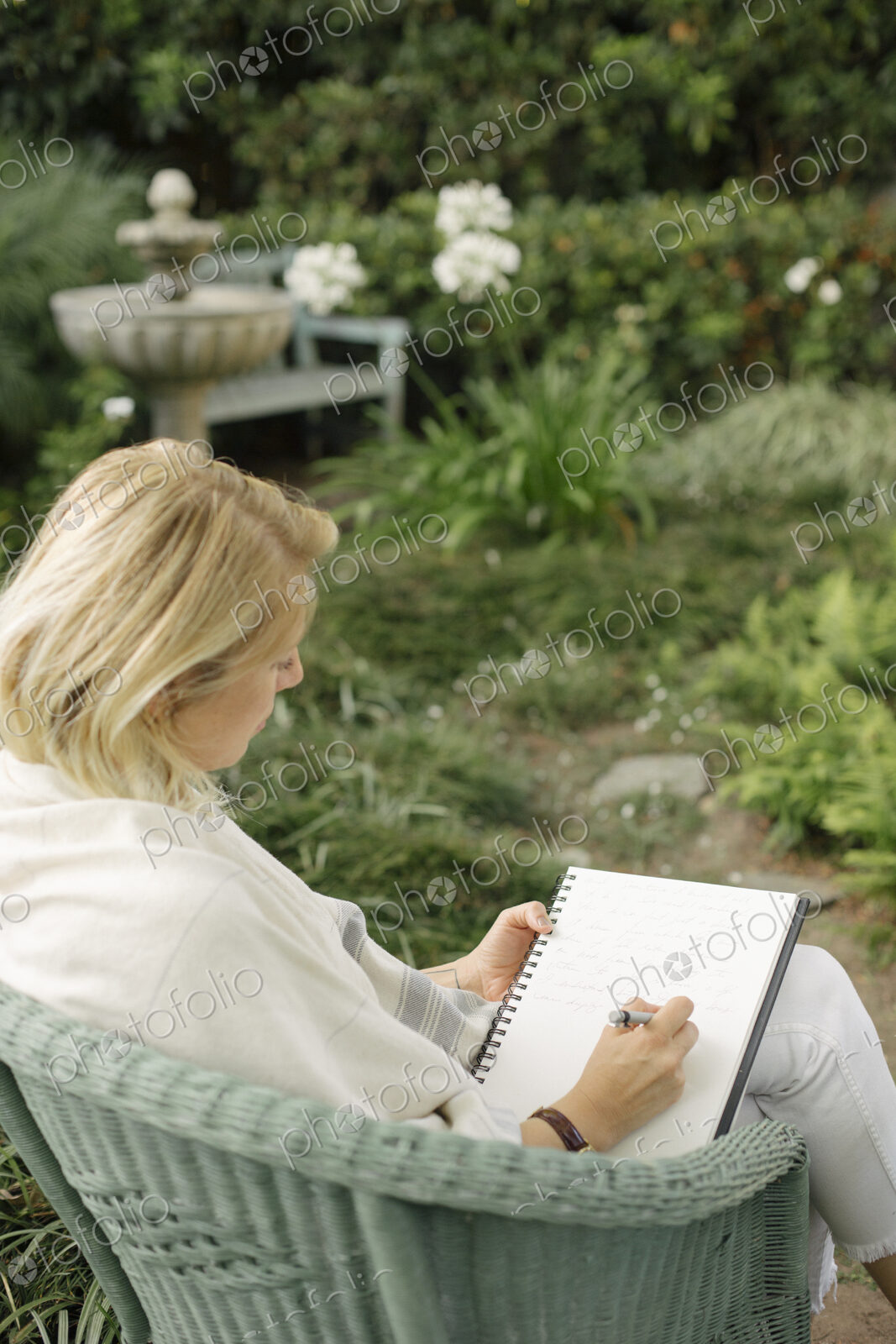 Blond woman sitting in a wicker chair in a garden, writing.