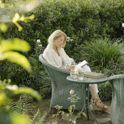 Blond woman sitting in a wicker chair in a garden, writing. Blond woman sitting in a wicker chair in a garden, writing.