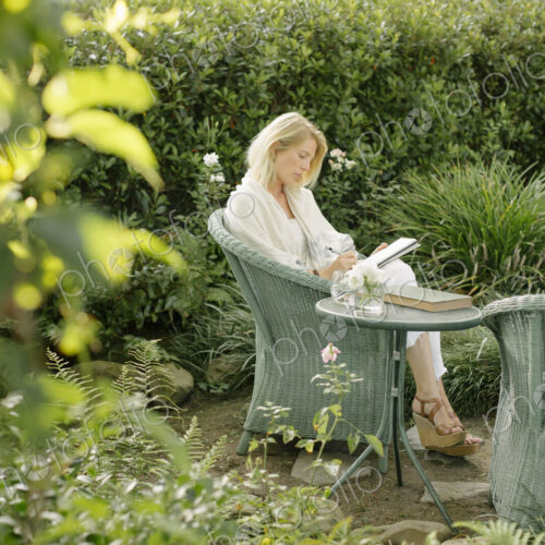 Blond woman sitting in a wicker chair in a garden, writing. Blond woman sitting in a wicker chair in a garden, writing.