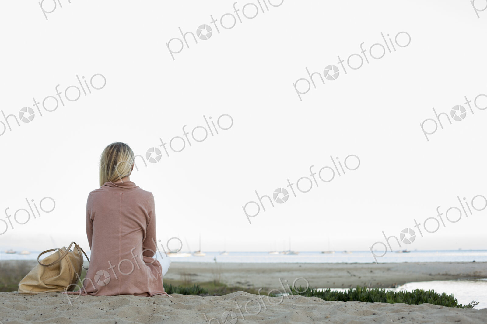 Blond woman sitting on a sandy beach.