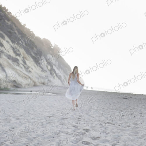 Blond woman walking on a sandy beach near a cliff. Blond woman walking on a sandy beach near a cliff.
