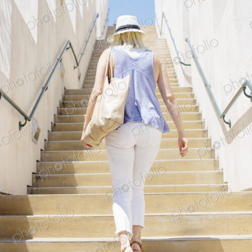 Blond woman wearing a hat walking up a staircase.