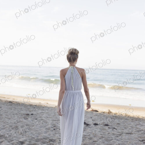 Blond woman wearing a long dress standing on a sandy beach. Blond woman wearing a long dress standing on a sandy beach.