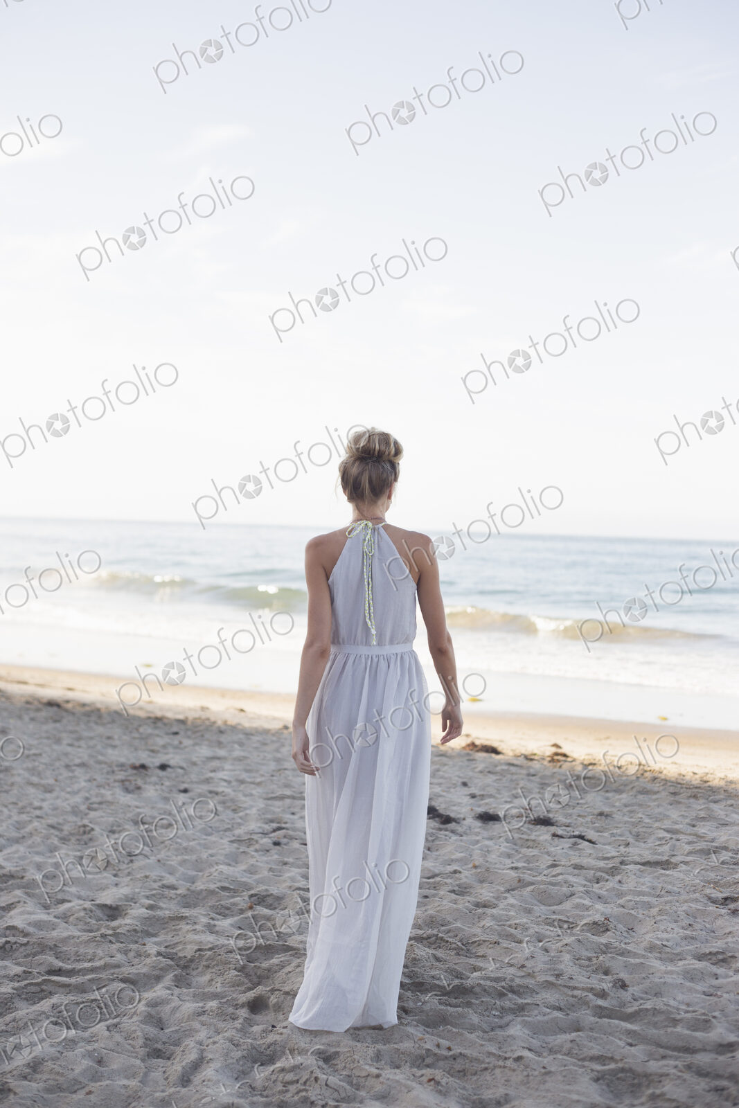 Blond woman wearing a long dress standing on a sandy beach.