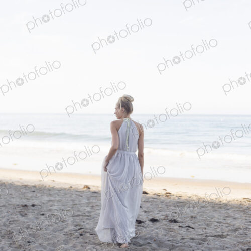 Blond woman wearing a long dress standing on a sandy beach. Blond woman wearing a long dress standing on a sandy beach.