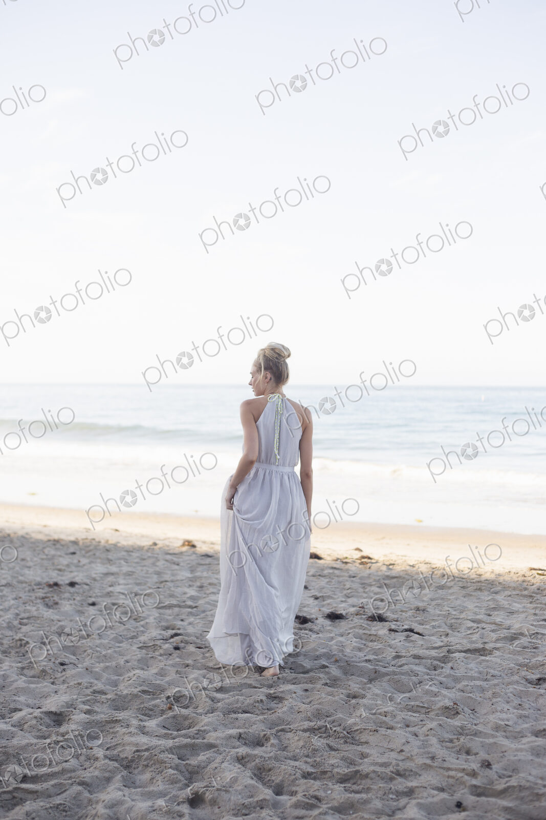 Blond woman wearing a long dress standing on a sandy beach.