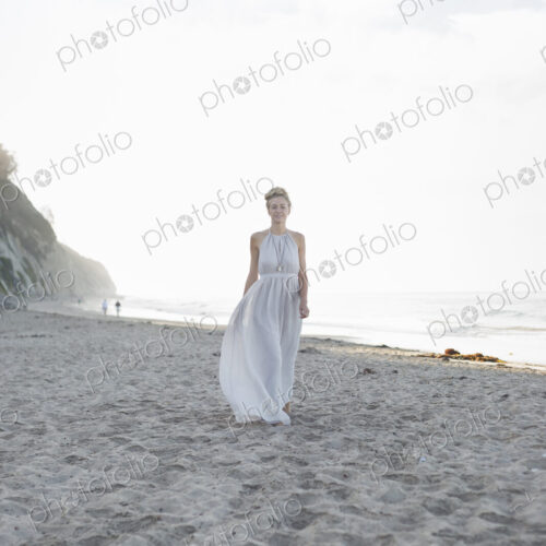 Blond woman wearing a long dress standing on a sandy beach. Blond woman wearing a long dress standing on a sandy beach.