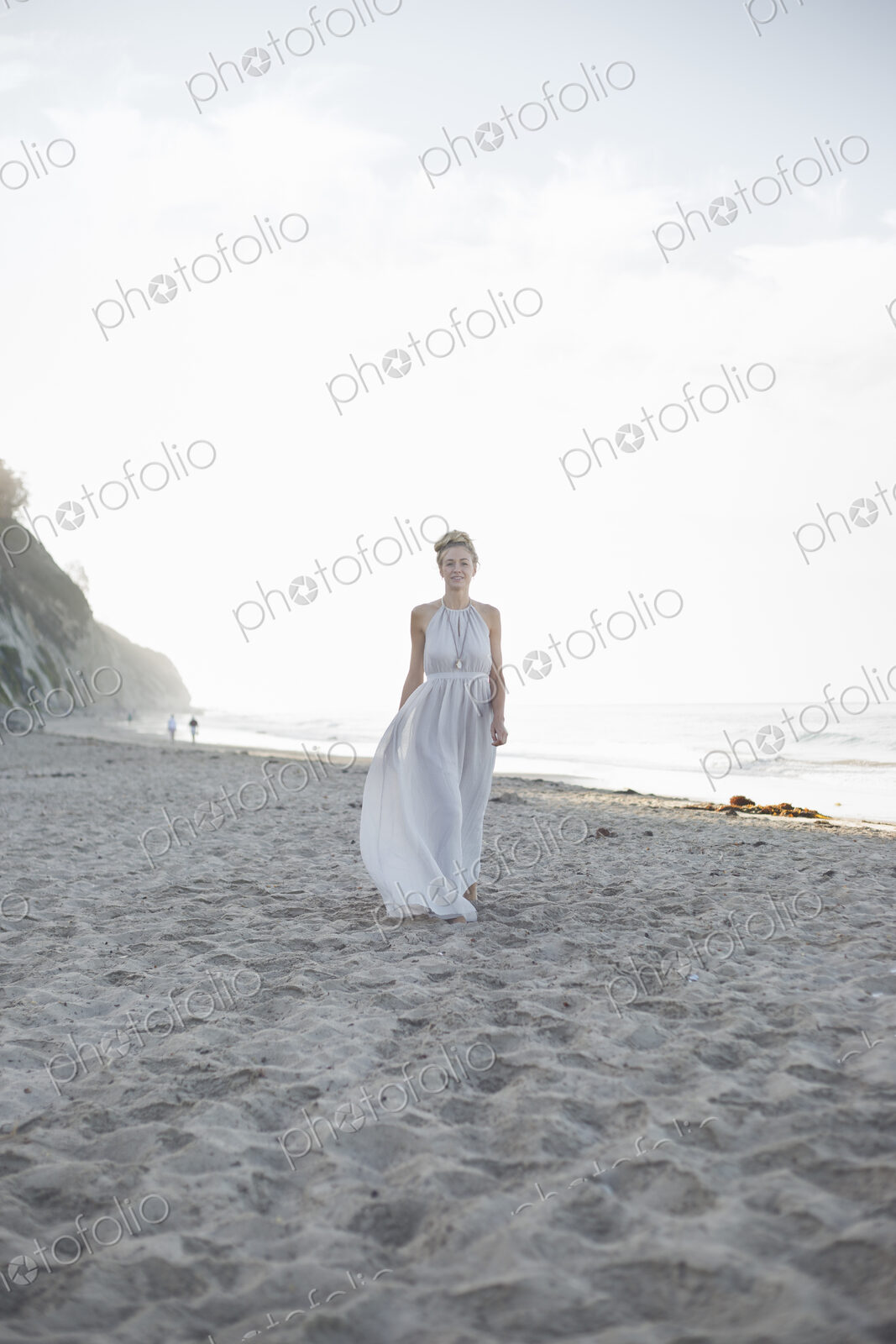 Blond woman wearing a long dress standing on a sandy beach.