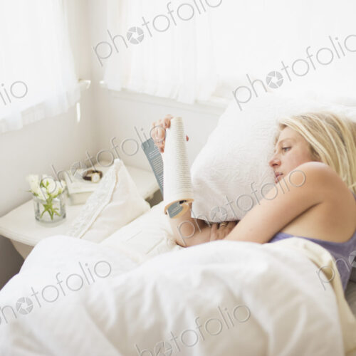 Blonde woman reading in a bed with white linen.