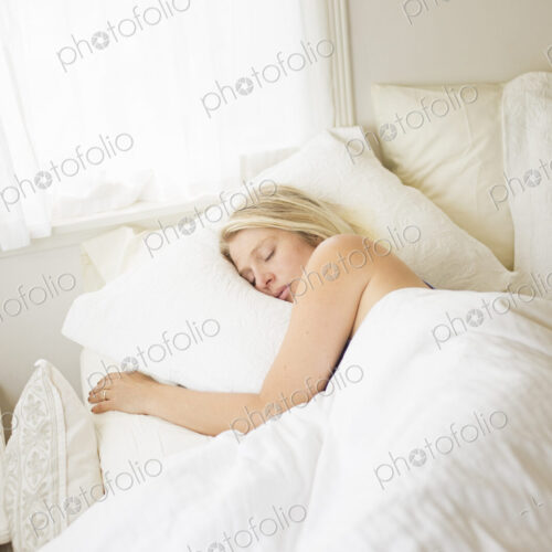 Blonde woman sleeping in a bed with white linen.