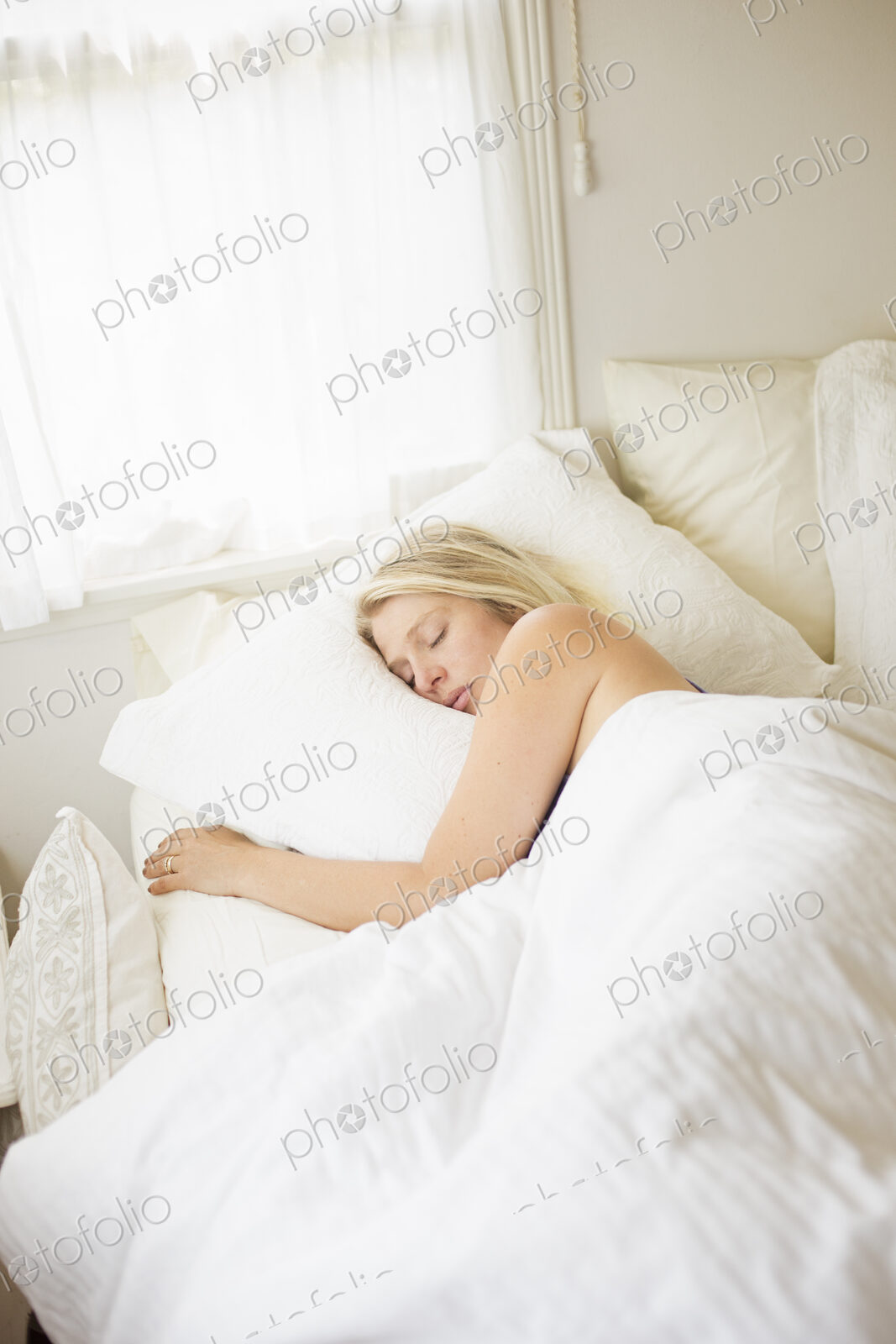 Blonde woman sleeping in a bed with white linen.