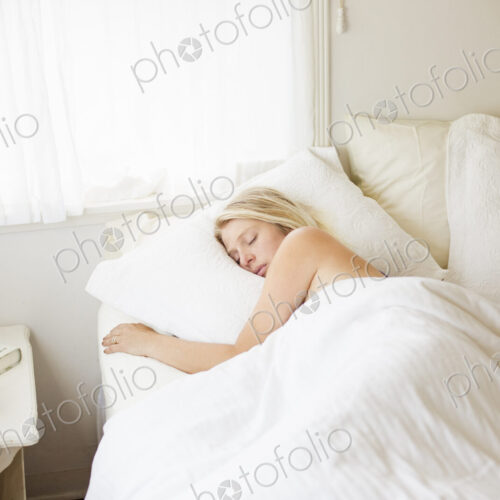 Blonde woman sleeping in a bed with white linen.