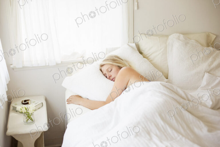 Blonde woman sleeping in a bed with white linen.