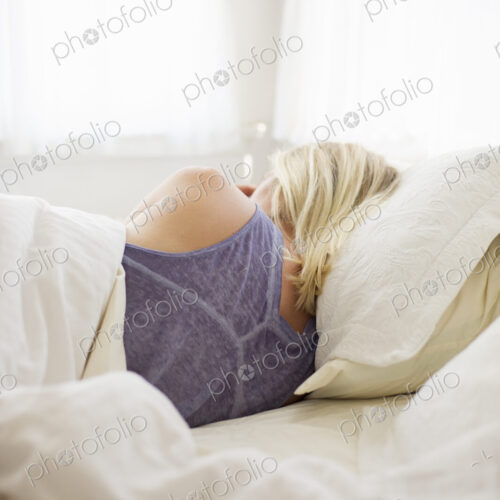 Blonde woman sleeping in a bed with white linen.