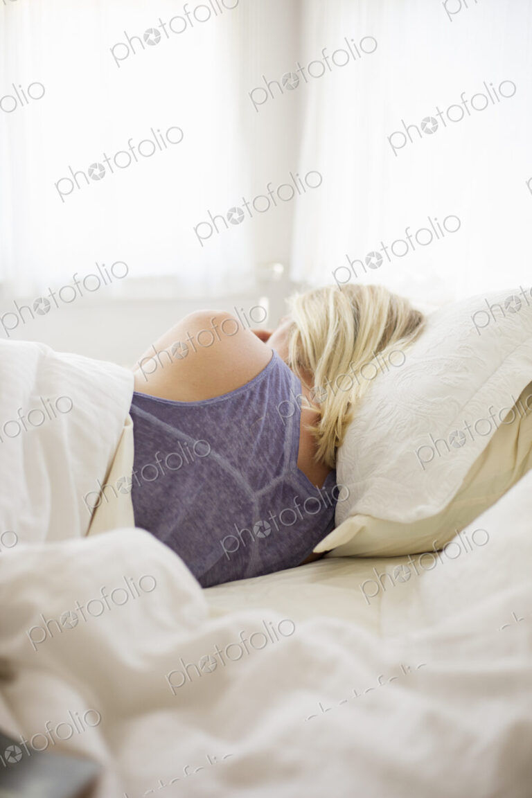 Blonde woman sleeping in a bed with white linen.