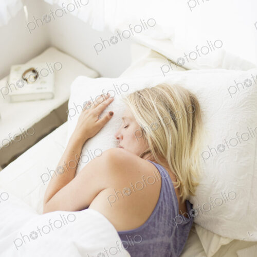 Blonde woman sleeping in a bed with white linen.