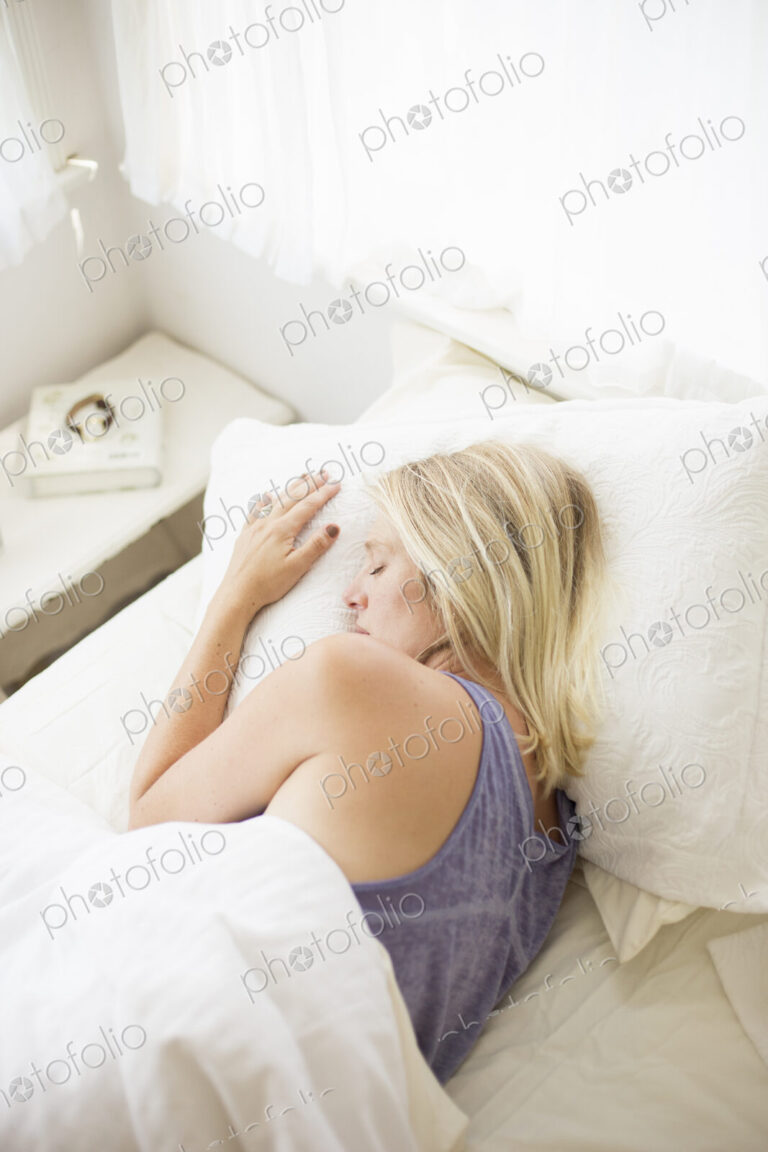 Blonde woman sleeping in a bed with white linen.