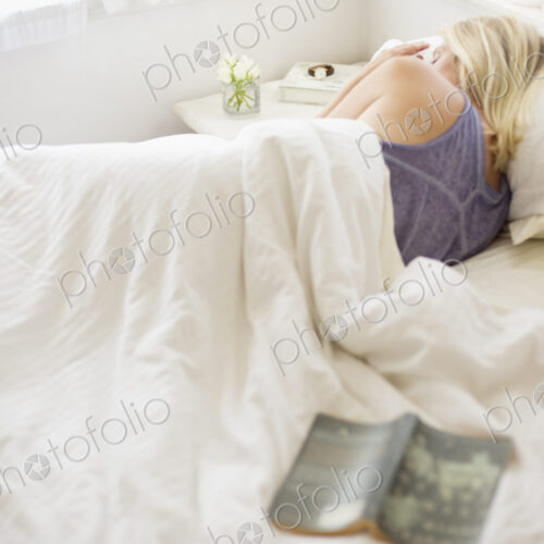 Blonde woman sleeping in a bed with white linen.