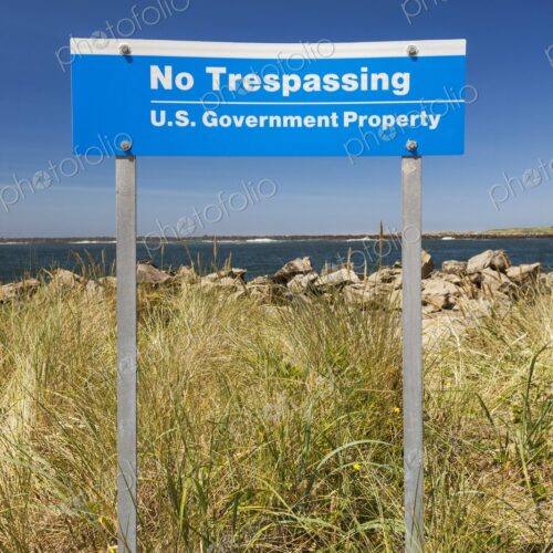 Blue "No Trespassing, U.S. Government Property" sign posted in grassy dunes near the… Blue "No Trespassing, U.S. Government Property" sign posted in grassy dunes near the…